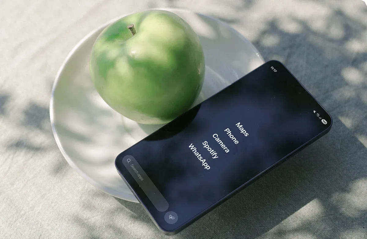 A Balance Phone lying on a table beside a bowl with a green apple, its screen showing a short list of apps